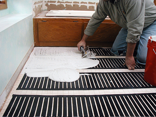 Thinset being applied over the heating element in a bathroom installation